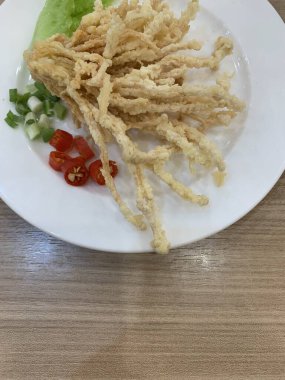 Çıtır çıtır kızarmış enoki mantarları, yanında taze marul dilimlenmiş yeşil soğan ve doğranmış kırmızı biber ile birlikte beyaz tabakta düzenlenir.. 