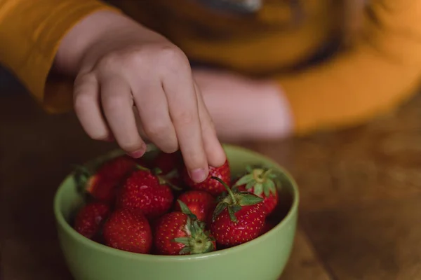 Close-up of a child\'s hand picking strawberries from a bowl. High angle
