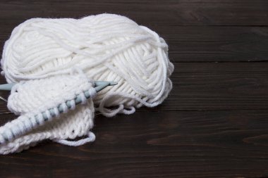 Hasır sepette örgü iğneleriyle bobinlerdeki yün iplikleri açık arkaplanda.