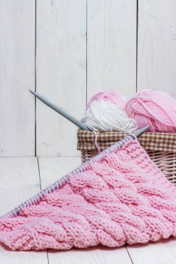 Hasır sepette örgü iğneleriyle bobinlerdeki yün iplikleri açık arkaplanda.