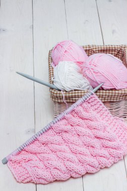 Hasır sepette örgü iğneleriyle bobinlerdeki yün iplikleri açık arkaplanda.