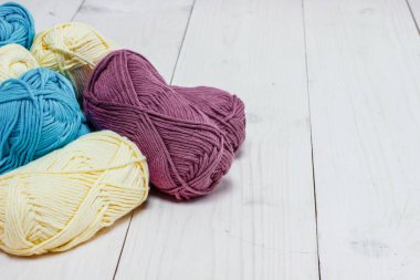 Hasır sepette örgü iğneleriyle bobinlerdeki yün iplikleri açık arkaplanda.