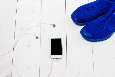 Spor ayakkabılar, kulaklıklar ve ahşap arka planda telefon..