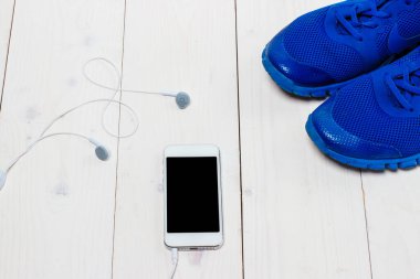 Spor ayakkabılar, kulaklıklar ve ahşap arka planda telefon..