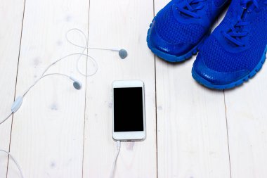 Spor ayakkabılar, kulaklıklar ve ahşap arka planda telefon..