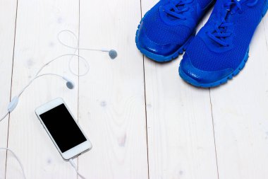 Spor ayakkabılar, kulaklıklar ve ahşap arka planda telefon..