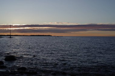 Gün batımında sakin bir liman. Güneş ufukta batıyor. Suyun üzerine sıcak bir parıltı saçıyor..