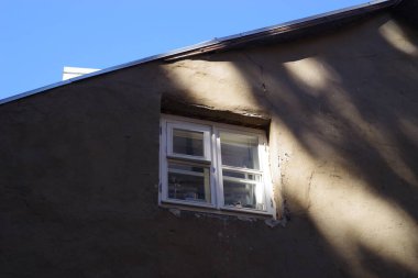 Beyaz pencere çerçeveli kahverengi bir bina, ikinci katta küçük bir dikdörtgen pencere ve üzerinde geniş açık bir alan..