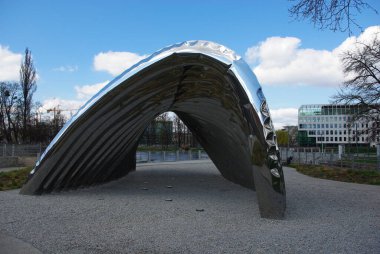 Bir park alanında altında açık bir alan olan modern, eğri bir metal heykel.