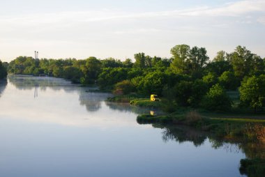 Sakin suları, yeşil bitki örtüsü ve berrak gökyüzü olan sakin bir nehir manzarası..