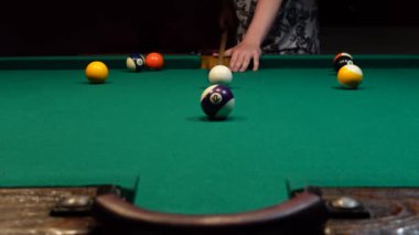 Adam bilardo topuna ıstakayla vuruyor. Top bilardoda başka bir topla çarpışıyor. Bilardo, bar, dinlenme.