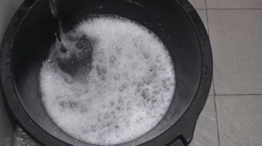 water flowing from the faucet on the laundry detergent makes foam in a bucket in preparation for washing clothes