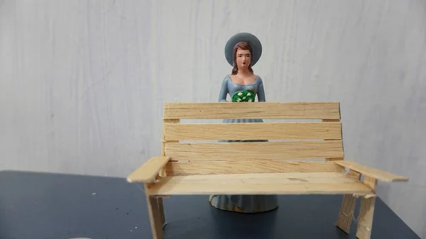 Selective focus Miniature toy doll women in dress with hat and handicrafts bench chair from ice cream wood              