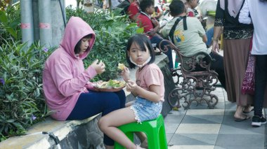 İki kız yaya geçidinde yol kenarındaki yiyeceklerden hoşlanıyordu. Surabaya, Doğu Java, Endonezya. 18 Aralık 2022