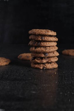 Siyah arka plandaki tahta masada bir yığın çikolatalı kurabiye.