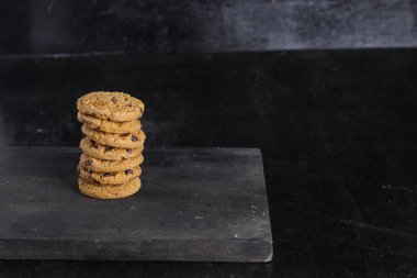Siyah arka plandaki tahta masada bir yığın çikolatalı kurabiye.