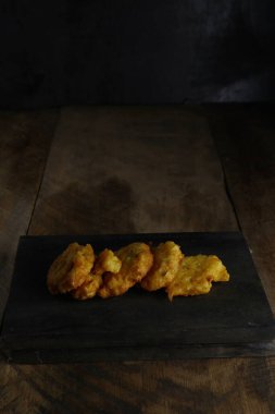 Bakwan Jagung ya da mısır böreği, tahta bir arka planda siyah bir kesme tahtasının üzerinde.