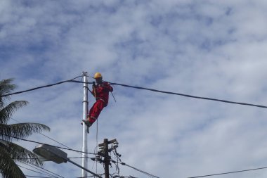 Gorontalo-Endonezya, Aralık 2022 - Teknisyenler elektrik direklerine kablolar bağlar. Düşük voltajlı kablo döşediği için elektrik direğinde kemerle asılı duran bir çalışan.