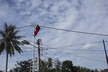 Gorontalo-Endonezya, Aralık 2022 - Teknisyenler elektrik direklerine kablolar bağlar. Düşük voltajlı kablo döşediği için elektrik direğinde kemerle asılı duran bir çalışan.