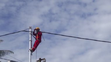 Gorontalo-Endonezya, Aralık 2022 - Teknisyenler elektrik direklerine kablolar bağlar. Düşük voltajlı kablo döşediği için elektrik direğinde kemerle asılı duran bir çalışan.