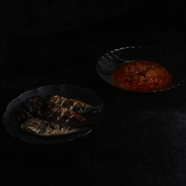 Siyah arka planda ızgara balık ve acı sos.