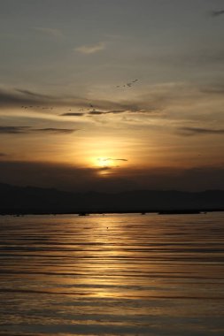 Suyun üzerinde gün batımı ve arka planda dağlar.