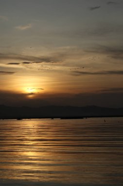 Suyun üzerinde gün batımı ve arka planda dağlar.