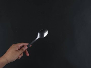Siyah arka planda izole edilmiş bir kaşığı tutan el.