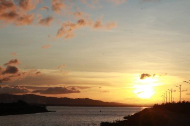 Arka planda Dağlar ve Bulutlarla Gölün Üzerinden Gün Batımı