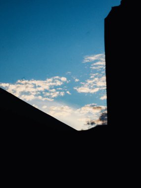 Mavi gökyüzü ve beyaz bulutlu bir evin silüeti.