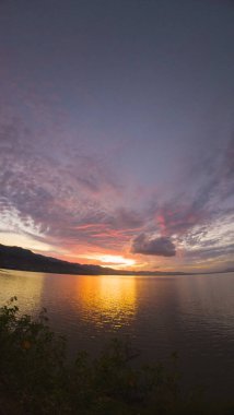 Sunset over the lake with dramatic clouds and mountains in the background clipart