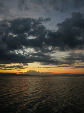 Arka planda dramatik bulutlar ve dağlarla gölün üzerinde gün batımı