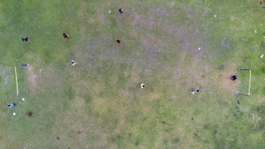 Halk parkındaki yeşil çimlerde futbol oynayan insanların hava görüntüsü