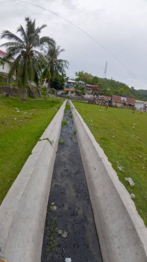 Bahçede kirli su ve yeşil çimen olan beton drenaj borusu.