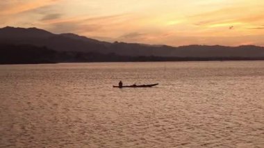 Gün batımında gölde bir balıkçı teknesinin silueti.