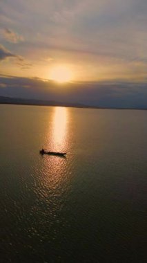 Gölde gün batımı ön planda bir tekne ve arka planda bir dağ.