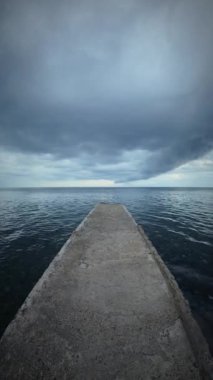 Fırtınalı bir gökyüzünün altında denizin ortasında beton iskele.