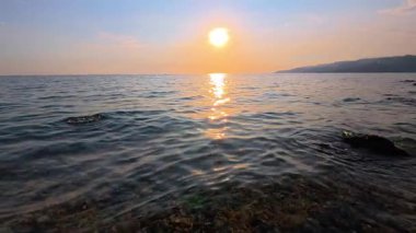 Denizde güzel bir gün batımı, dalgalar ve çakıl taşı plajı. Yavaş çekim