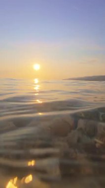 Denizde güzel bir gün batımı, dalgalar ve çakıl taşı plajı.