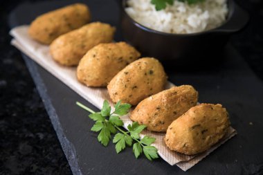 Bolinhos de bacalhau, Portekiz gastronomisiyle ünlüdür. Kızarmış hamur köftesi, morina köftesi, balık, tuzlu morina böreği, bacalao bunuelos. Siyah arka planda beyaz pirinçli morina balığı keki..