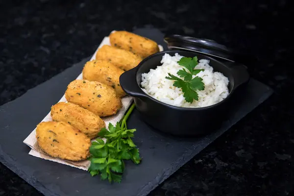 Bolinhos de bacalhau, very famous in Portuguese gastronomy. Fried dumpling, cod dumpling, fish, salted cod fritters, bacalao bunuelos. Codfish cake served with white rice on a dark background.