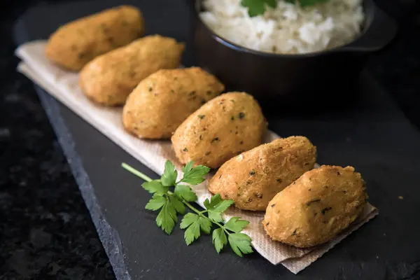 Bolinhos de bacalhau, Portekiz gastronomisiyle ünlüdür. Kızarmış hamur köftesi, morina köftesi, balık, tuzlu morina böreği, bacalao bunuelos. Siyah arka planda beyaz pirinçli morina balığı keki..