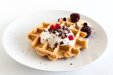 Lezzetli ev yapımı yulaf ezmeli waffle kremalı doğal yoğurt, bal, muz, yabanmersini, ahududu ve beyaz arka planda doğranmış çikolata..