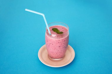 Mavi zemin üzerinde uzun bir bardakta karışık kırmızı meyveler bulunan vitamin ve antioksidanlarla dolu taze ve lezzetli bir içecek. Naneli kırmızı meyve püresi. Boşluğu kopyala.