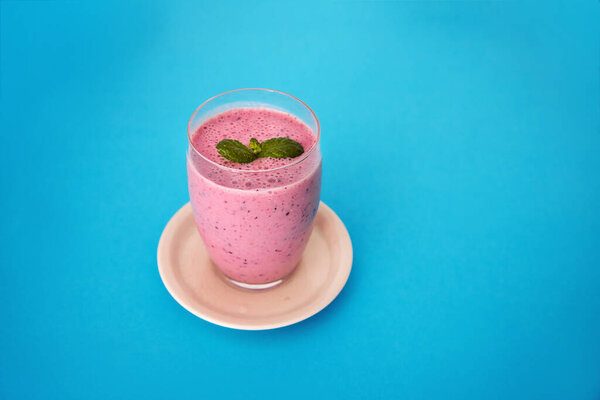 Fresh and delicious drink full of vitamins and antioxidants based on mixed red fruits in a tall glass on a blue background. Red fruit smoothie with mint. Copy space.
