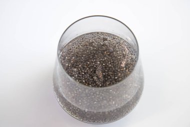 Edible chia seeds from the Salvia hispanica plant. Very healthy functional food to use in various recipes. Glass cup containing the hydrated seeds. Image seen from above on white background. clipart