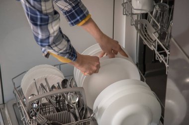 Bulaşık makinesi açık ve bir kişi bulaşıkları yıkıyor. Günlük aktivitelerde su ve zaman tasarrufu kavramı.