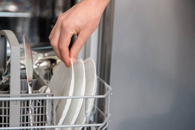 Bulaşık makinesi açık ve bir kişi bulaşıkları yıkıyor. Günlük aktivitelerde su ve zaman tasarrufu kavramı.