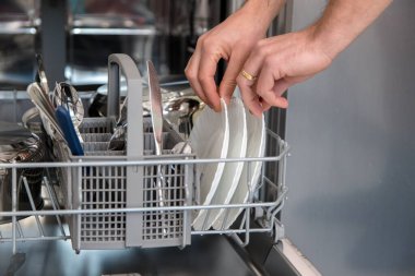 Bulaşık makinesi açık ve bir kişi bulaşıkları yıkıyor. Günlük aktivitelerde su ve zaman tasarrufu kavramı.