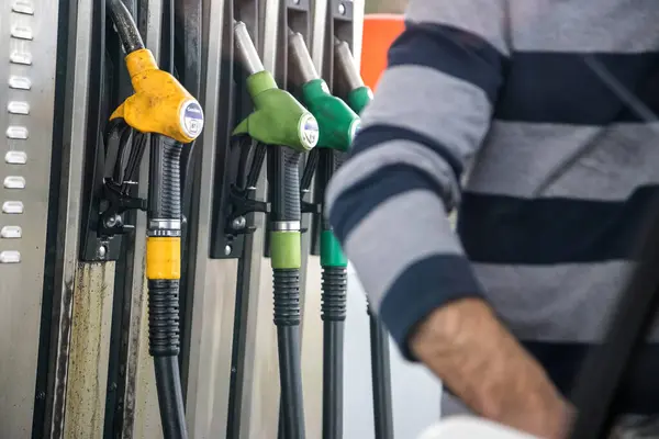 Yakıt deposunu dolduran kişi, arka plandaki farklı petrol ürünlerinin hortumlarını vurguluyor. Arkaplana odaklan.